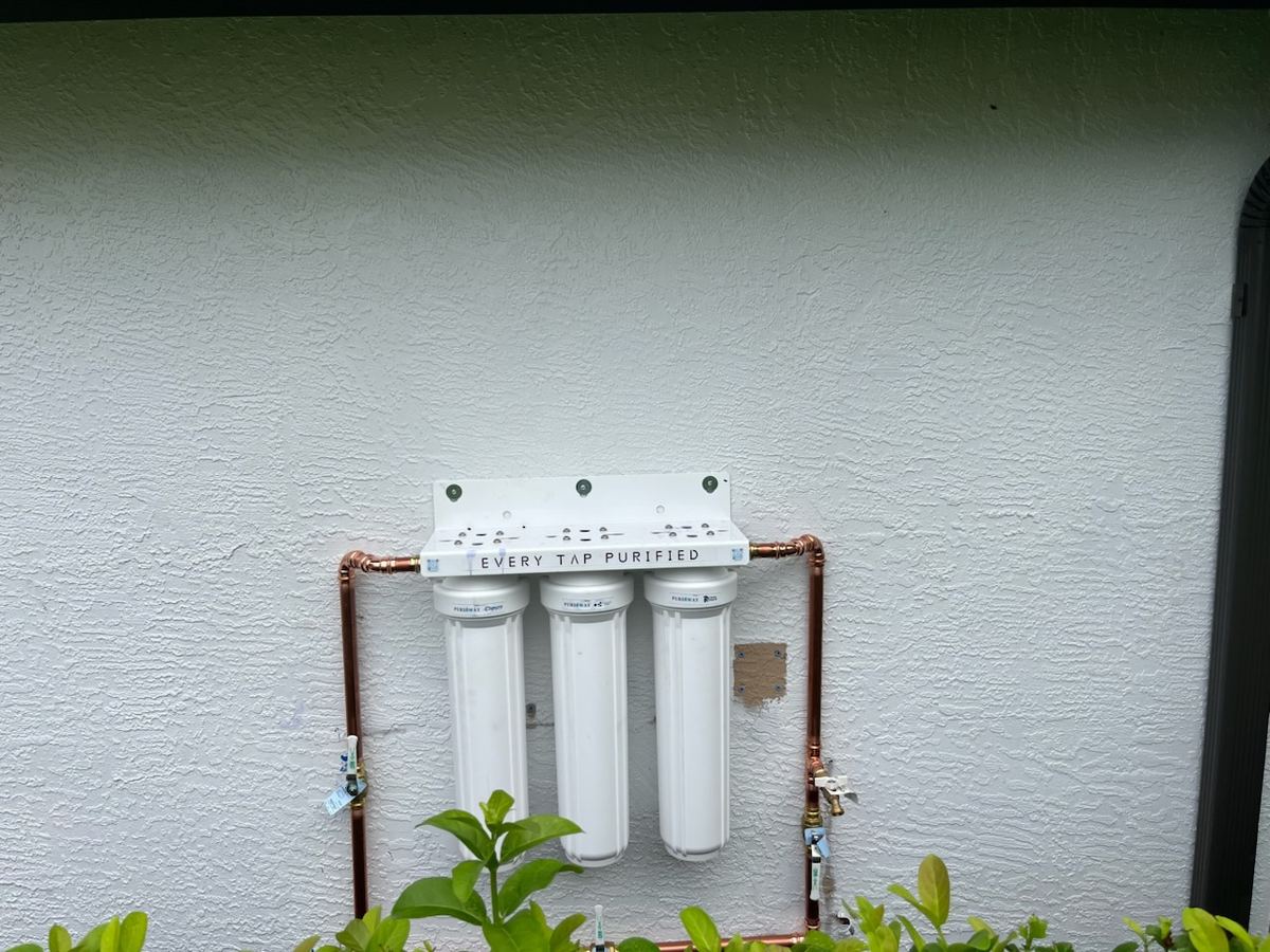 Whole-home water filtration system installed on a white wall with copper piping